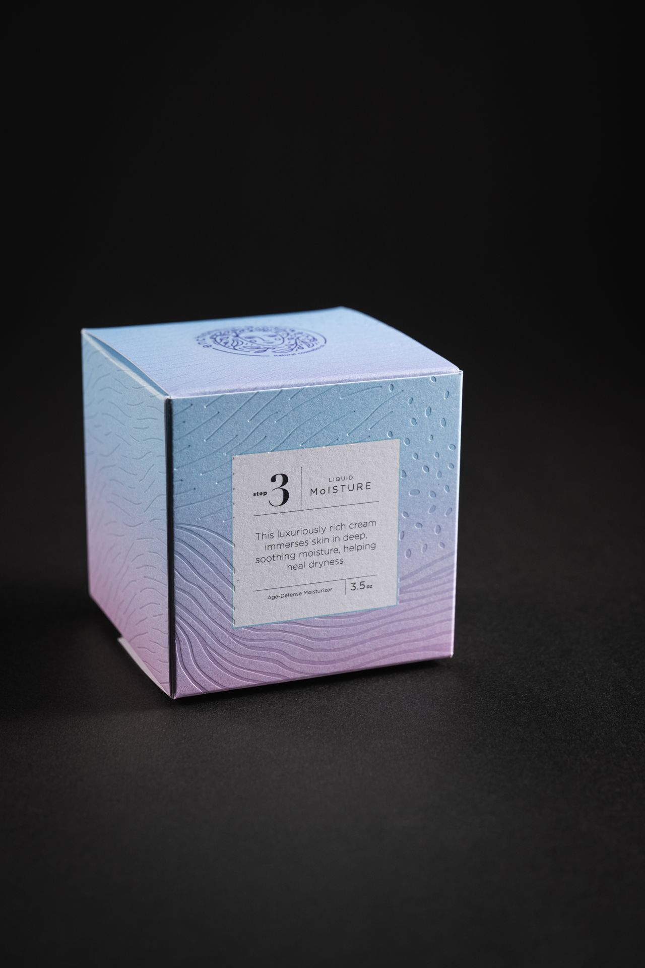 The Enchanting cosmetics carton — a blind-embossed wave pattern on a blue-to-lilac gradient stock.
